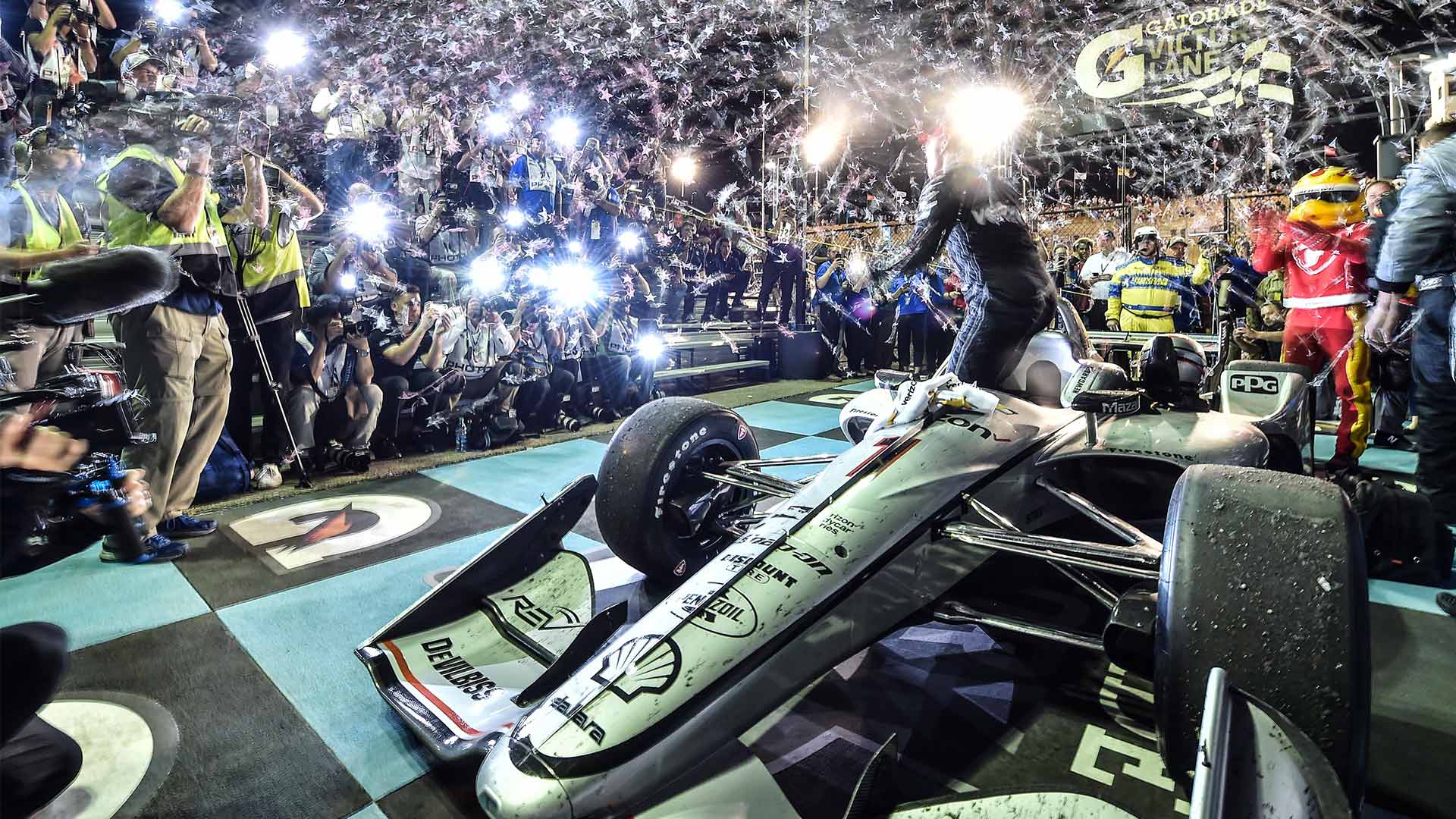 Cameras flashing and confetti flying as Josef Newgarden exits his car in victory circle